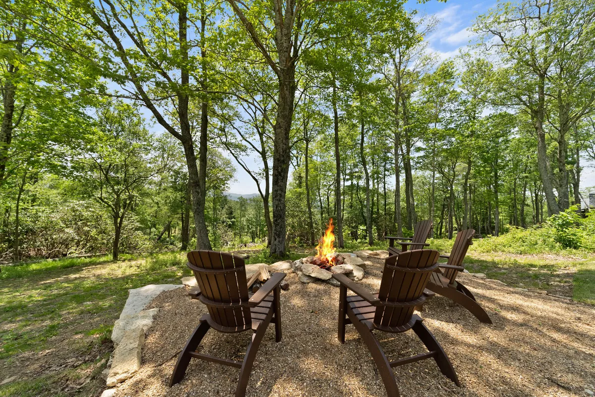 A cozy fire pit encircled by Adirondack chairs is set among tall trees, creating an inviting atmosphere for storytelling, marshmallow roasting, and unwinding beneath the stars.