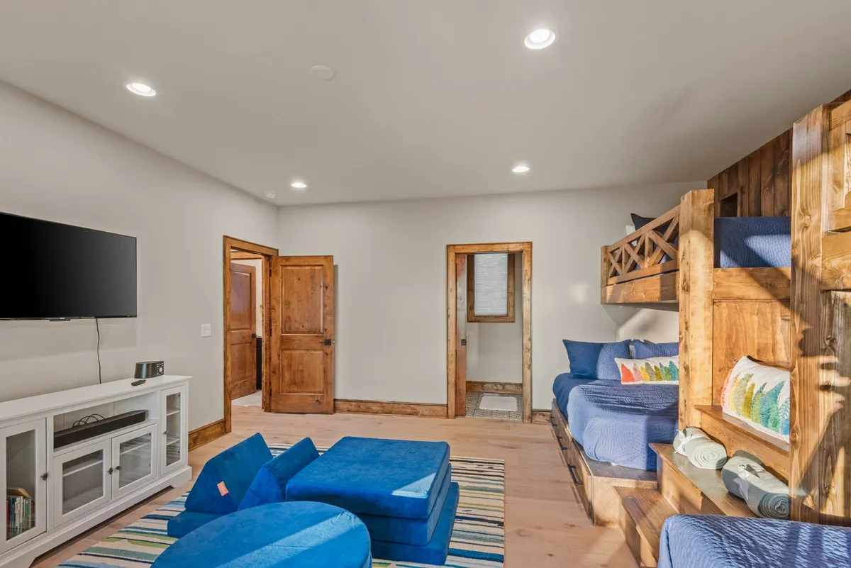 This interior scene features bunk beds, a blue seating area, and a television mounted at eye level—ideal for movie marathons and game nights. The layout is casual and inviting, structured for both group activities and quiet downtime.