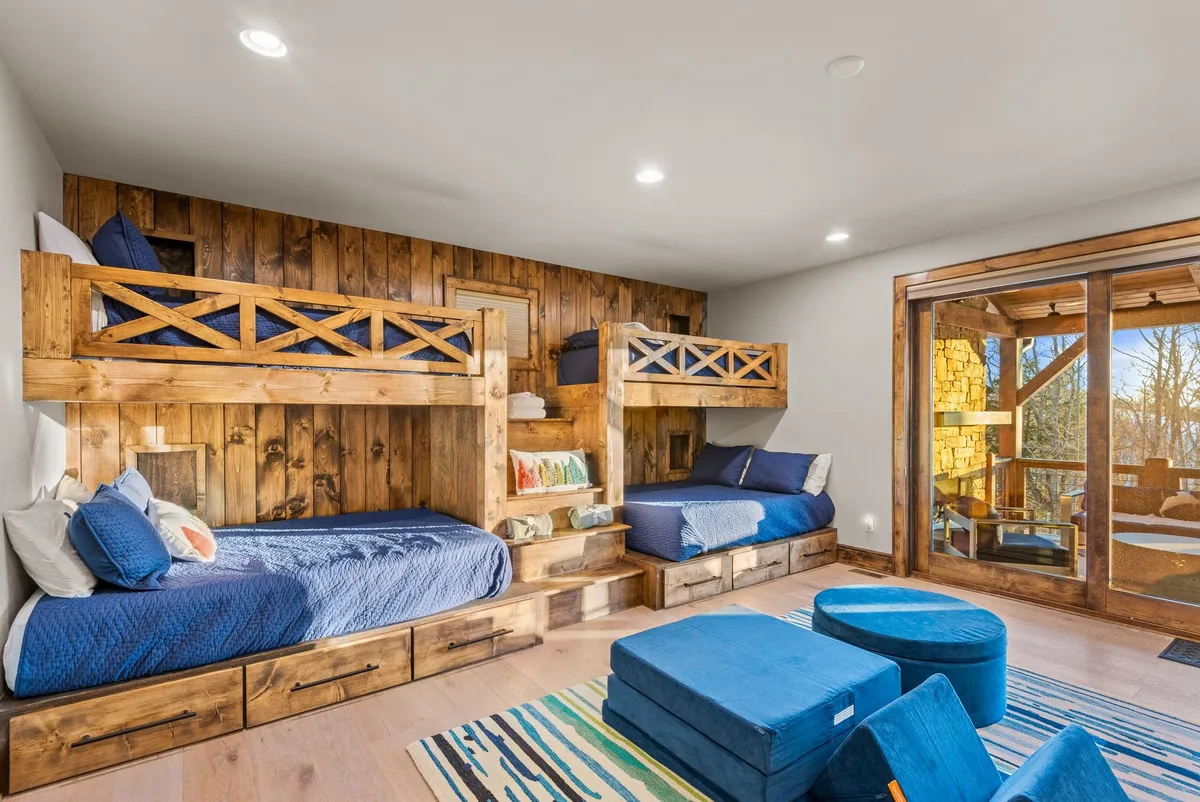 This image showcases a playful and cozy bunk room with two sets of bunk beds, bright blue seating, and warm wooden accents. The arrangement encourages both sleep and play, while the room is filled with cheerful, youthful energy.