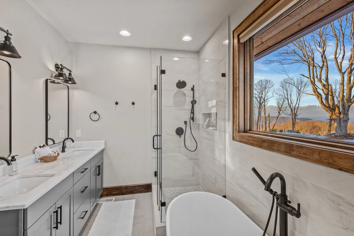 A luxurious bathroom with a freestanding soaking tub, a large walk-in shower, double vanity with mirrors, and a scenic window view. The space is modern and spa-like, perfect for self-care routines and relaxation after an adventurous day.