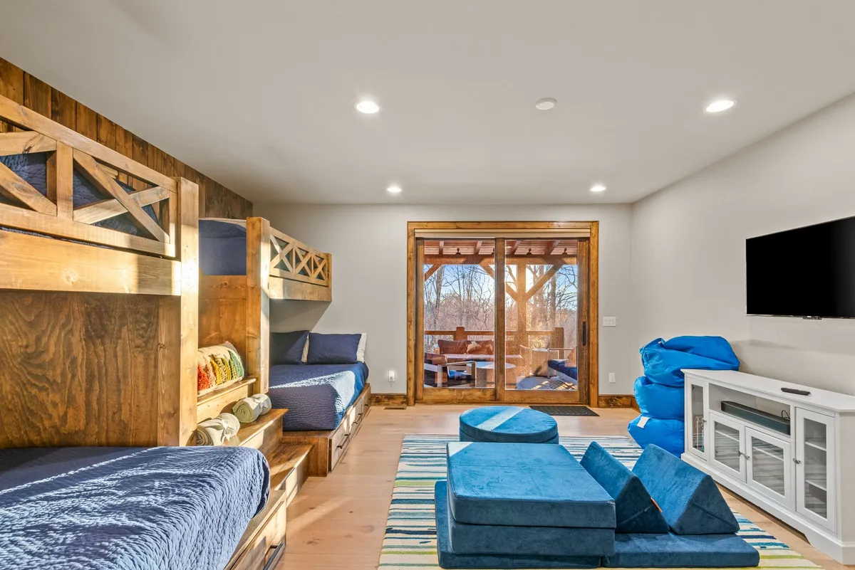 The image captures bunk beds, a blue seating area, and large glass doors opening to an outdoor space. The setting is ideal for both rest and play, with the doors hinting at easy access to the deck for outdoor adventures.