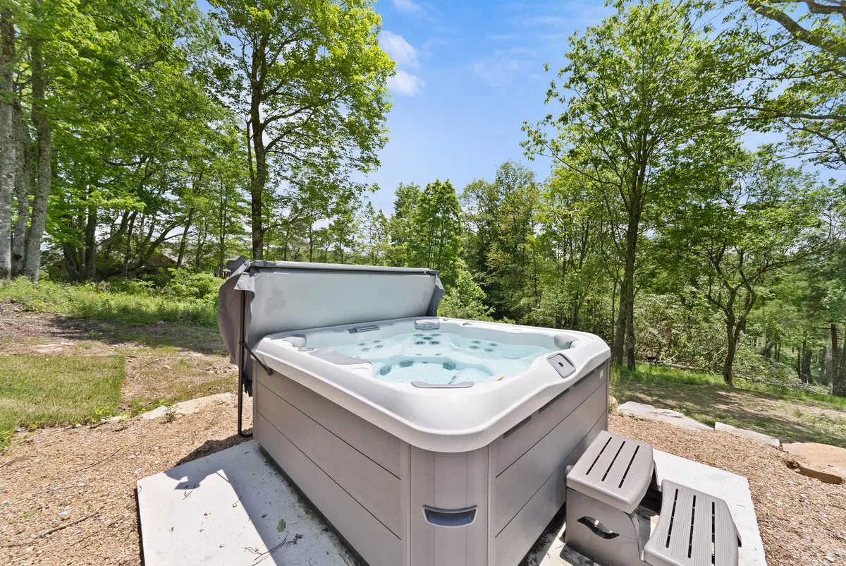 A tranquil patio setting with a bubbling hot tub surrounded by trees. The area promises relaxation and rejuvenation, with opportunities for stargazing or enjoying morning coffee in nature.