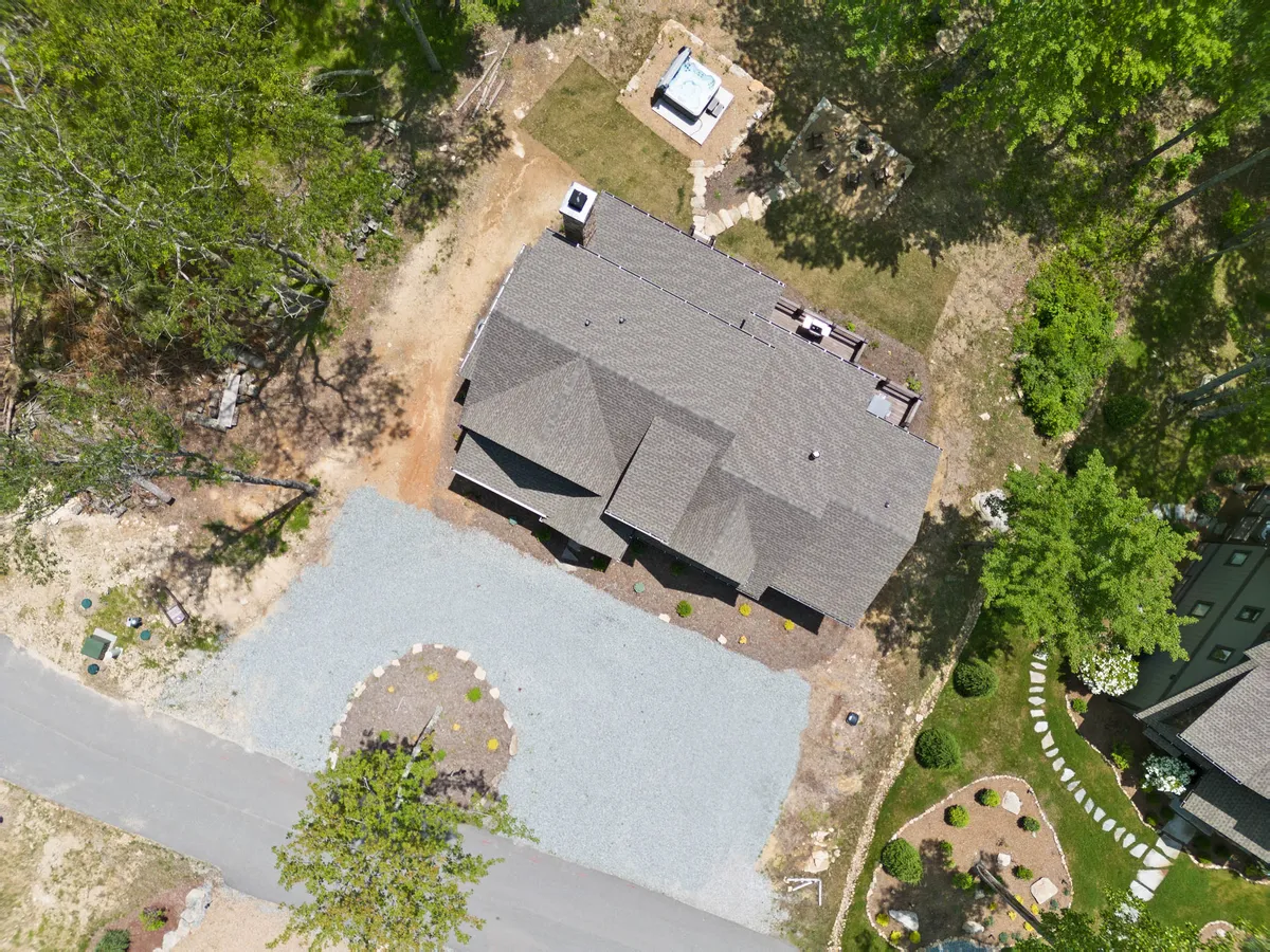 A wide view of the property exterior featuring a gravel driveway, lush greenery, and a patio area perfect for outdoor lounging. The spacious yard and patio highlight the kind of environment where dogs can play and owners can unwind.
