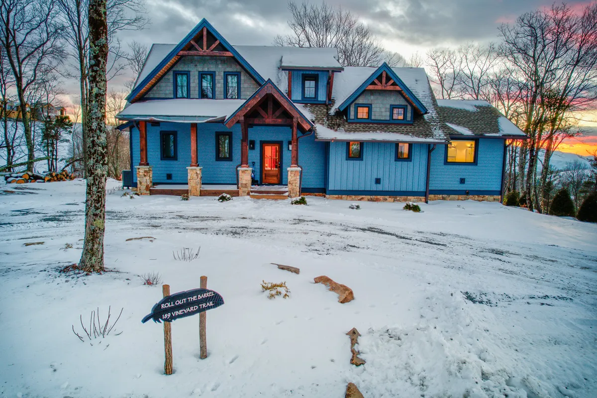 This exterior image highlights the blue house with a welcoming wooden porch, surrounded by a snow-covered landscape at sunset. There’s a visible signpost, and the sunset sky creates a tranquil, adventurous atmosphere ideal for winter activities and exploration.