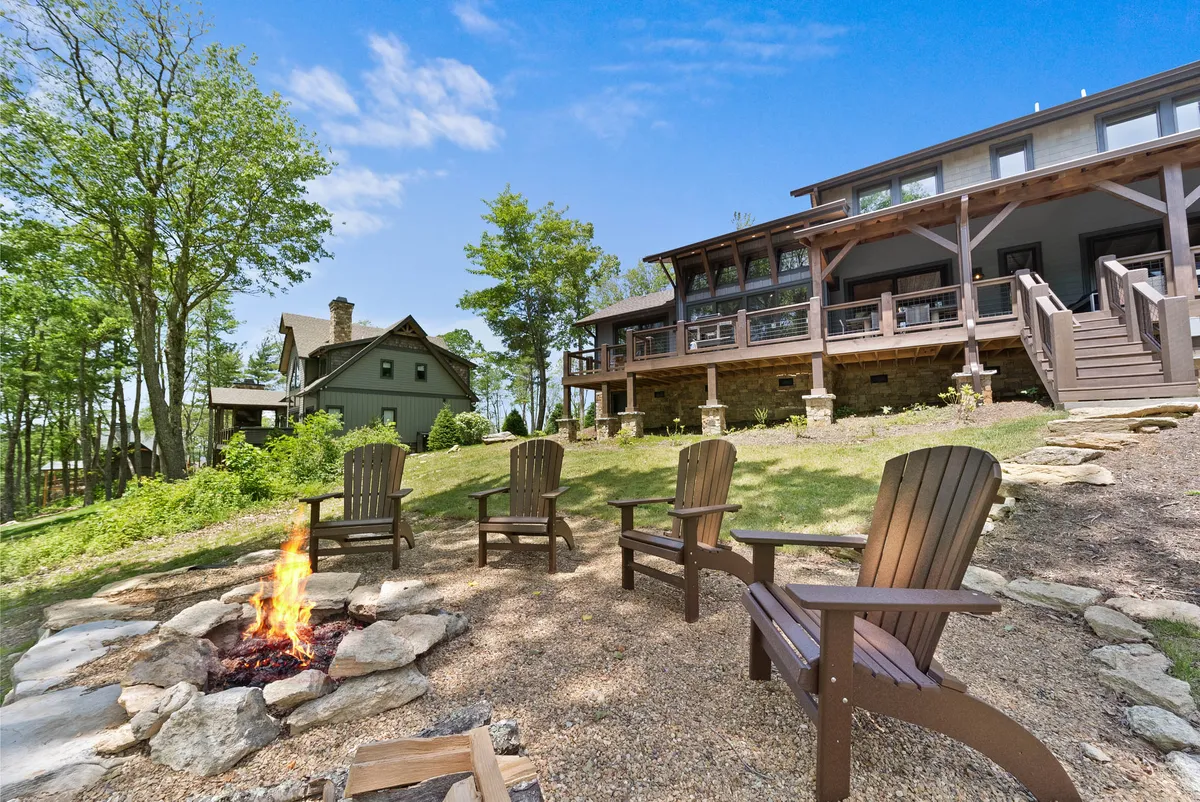 A cozy fire pit encircled by Adirondack chairs, set against the main house and a backdrop of trees. The setting is ideal for stargazing, storytelling, or sharing s'mores with family and friends.